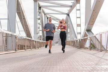 Young adult friends doing a morning marathon in the morning outdoor. Man and woman jogging together with sport wear and smiling in a sunny day