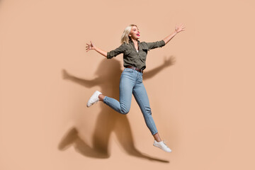 Fototapeta na wymiar Full length photo of excited impressed woman dressed khaki shirt jumping high isolated beige color background