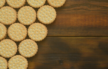 A round sandwich cookie with coconut filling lies in large quantities on a brown wooden surface. Photo of edible treats on a wooden background with copy space