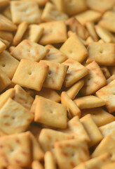 A lot of small cookies are square shaped. A pattern of a yellow salt cracker. Background image with salted pastry