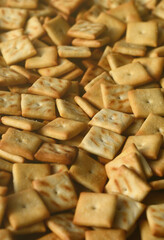 A lot of small cookies are square shaped. A pattern of a yellow salt cracker. Background image with salted pastry