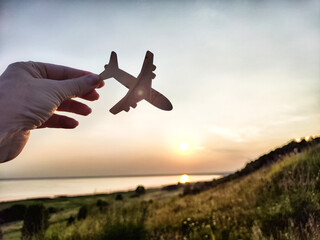 Hand holding toy wooden airplane plane and blue sky with sun during sunset. Plane flying down...