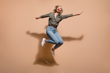 Fototapeta na wymiar Full length photo of excited shiny lady wear khaki shirt jumping high isolated beige color background