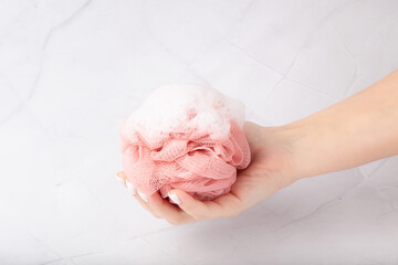 Female hand holds bath sponge with white lush foam - obrazy, fototapety, plakaty