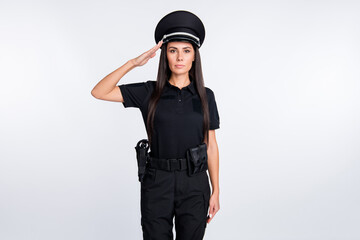 Photo of serious charming young policewoman dressed black clothes saluting arm headwear isolated white color background