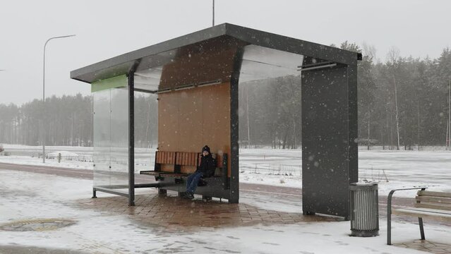 Lost child sits on empty public transport bench on winter day, wide shot. Unattended child has lost his way to house on outskirts of the city and is waiting for help.