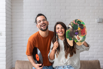 Young creative couple, artists musician and painter holding LP and colors palette with painting...