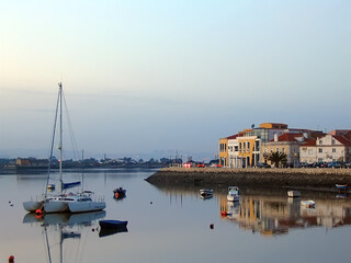 Fototapeta na wymiar Seixal City and Seixal Bay view with small boats and a sailing trimaran at twilight, nightfall, dusk or evening. Setubal, Portugal