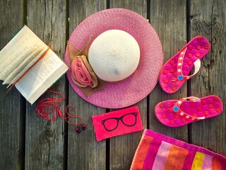 Summer flat lay including a straw hat, sunglasses, flip flops, headphones and a book placed on a...