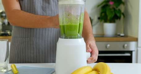 Man mixing bananas and spinach for delicious smoothie into blender