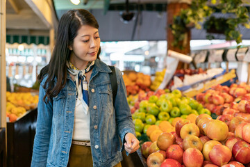 Portrait of a smiling attractive young woman buyer in the supermarket looking around fresh apples...