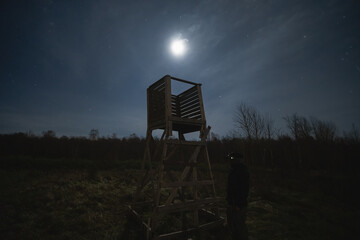 A man with a night vision device at a hunting tower at night in the forest, photo with low lighting.