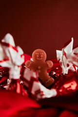 a figurine of a gingerbread man stay on a red silk fabric among Christmas red candies, christmas decorations