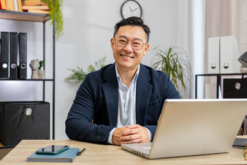 Portrait of happy smiling Asian businessman at modern home office workplace desk looking at camera....