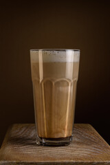 coffee with foamed cream in a ribbed transparent glass with long highlights stands on a board on a brown soft background with a gradient. artistic vertical shot