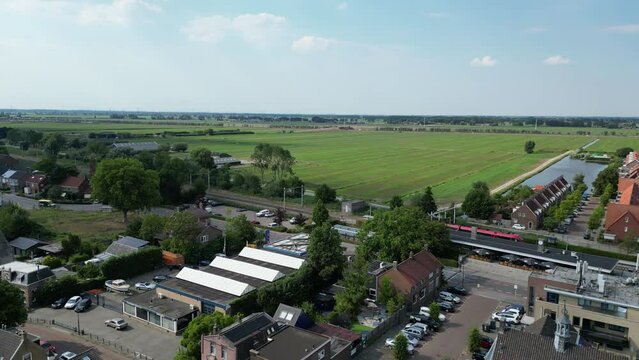 Dutch Red R-net Train Gliding Parallel to a Traffic Road in a Village on a Sunny Day in Holland