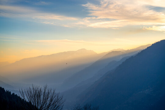 Serene peaceful view of himalaya mountains from Hamta village trek showing hues at dusk sunrise with sun rays passing between mountains in Manali