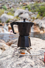 Black Mocha Pot on a gas burner in the mountains with a rock pool in the background