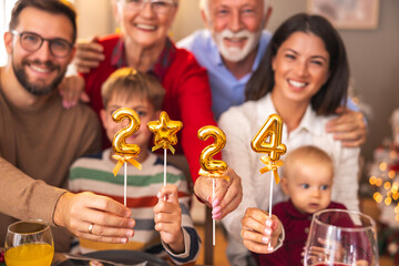 Family holding balloons shaped as numbers 2024 while having Christmas dinner at home
