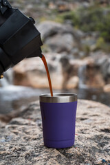Pouring Coffee into a camping mug by a rock pool in the mountains