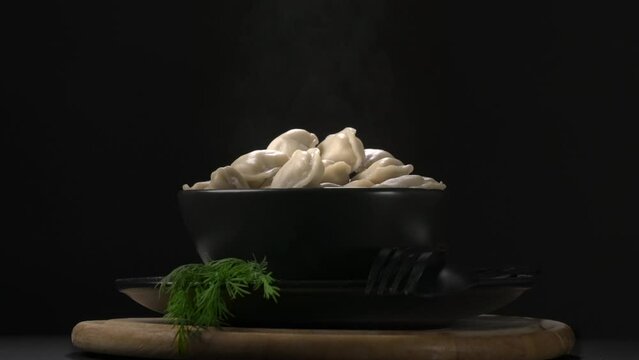 Hot dumplings in a black plate with smoke and dill on a dark background.