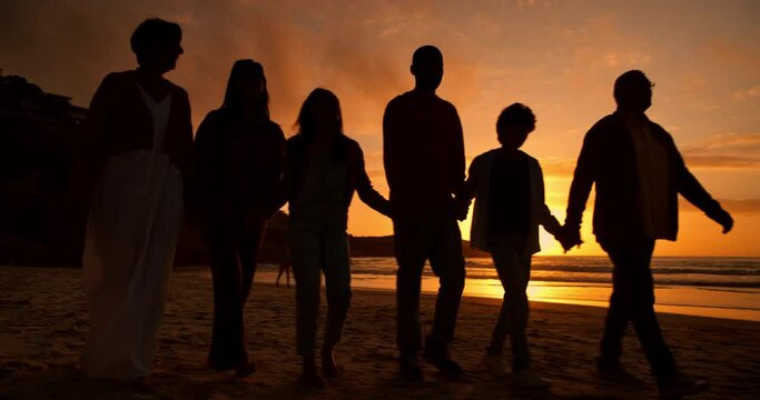 Sunset, walk and silhouette of family at the beach on a summer vacation, holiday or weekend trip. Travel, evening and shadow of people holding hands by the ocean or sea on tropical getaway together.