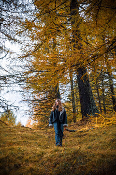 Young girl walking through forest in autumn colors of yellow and orange. Meran, South Tirol, Italy