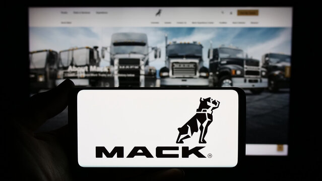 Stuttgart, Germany - 11-10-2023: Person holding smartphone with logo of US truck manufacturing company Mack Trucks Inc. in front of website. Focus on phone display.