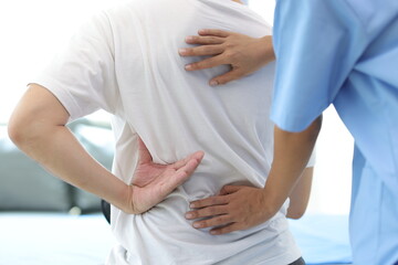 Doctor is diagnosing a male patient's back and lumbar pain in an examination room at a hospital.