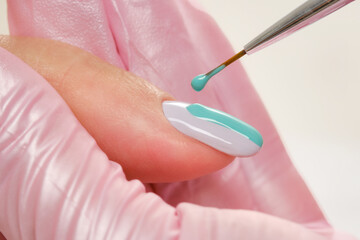 Close up process of applying varnish. Manicurist drawing on female nails. Nail green and blue...