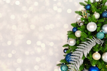Holiday Christmas tree with ornaments and balls on silver background with golden bokeh lights.