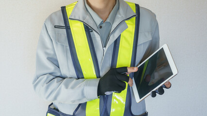 タブレットを持つ作業服の男性　指先がカットされた手袋で操作する