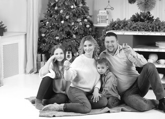 Obraz premium Black and white photo family on New Year's Eve with champagne sitting on the carpet. Mom, dad, son and daughter. Family celebration. Traditions concept
