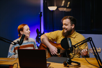 A cheerful couple of radio presenters perform a song on air. A man and a woman sing to the guitar...
