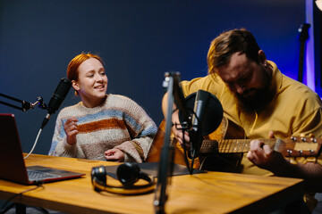 Obraz premium A cheerful couple of radio presenters perform a song on air. A man and a woman sing to the guitar in a home studio, creating content for their channel.