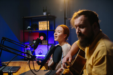 A cheerful couple of radio presenters perform a song on air. A man and a woman sing to the guitar...