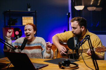 A cheerful couple of radio presenters perform a song on air. A man and a woman sing to the guitar in a home studio, creating content for their channel.