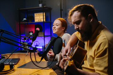 A cheerful couple of radio presenters perform a song on air. A man and a woman sing to the guitar in a home studio, creating content for their channel.