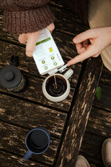 Man with long hair pouring coffee in a mug outside in nature by the river