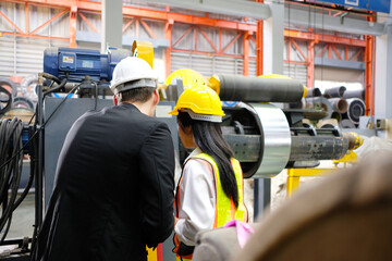 Male and female engineers wearing safety helmets inspect machinery in a factory.