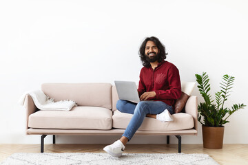 Joyful young indian guy in casual chilling with modern laptop