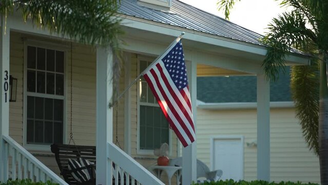 Florida suburban home with USA national flag waving on wind in front yard. American stars and stripes spangled banner as symbol of democracy