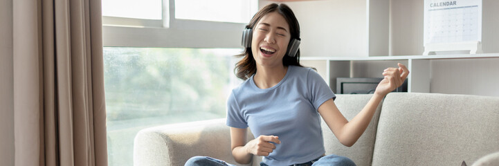 Naklejka premium Young Asian woman happily listening to music through headphones, Woman was enjoying listening to her favorite music and rocking to the beat of the music, Stress relief, Happiness in life.