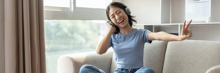 Young Asian woman happily listening to music through headphones, Woman was enjoying listening to her favorite music and rocking to the beat of the music, Stress relief, Happiness in life.
