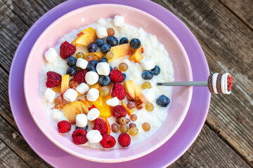 Oatmeal porridge with fruit, berries and mini marshmallow with spoon on wooden background table top view, homemade healthy breakfast cereal