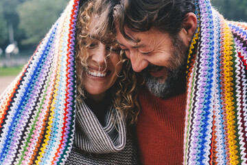 Obraz premium Overjoyed adult caucasian couple under a colorful cover laugh and have fun together with love and friendship. Young mature people in outdoor leisure romantic activity. Man and woman laughing a lot