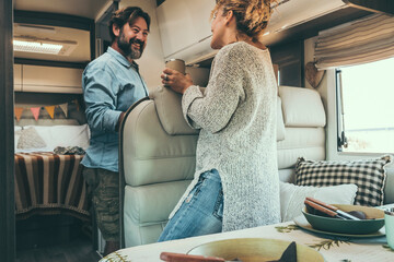 Happy adult couple enjoy vacation on camper van and prepare lunch together. Alternative travel lifestyle for modern people. Man and woman smile inside motor home. Van life and holiday trip vacation