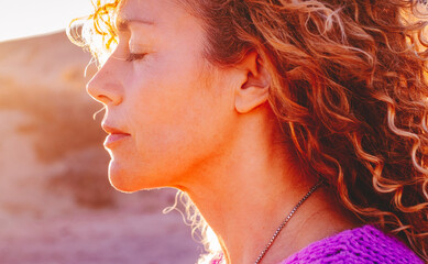 Close up sunset portrait of attractive woman with closed eyes and sun in back light. Dreaming and...