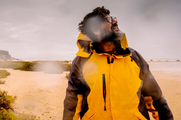 Standing explorer adventure man walking down the rain at the beach. Concept of bad weaterh nature and feeling. Male people with yellow jacket in outdoor leisure activity - obrazy, fototapety, plakaty
