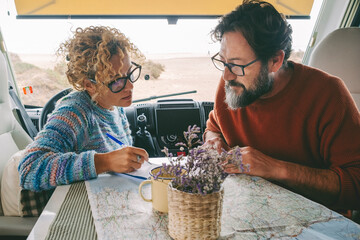 Adult couple planning next travel destination sitting inside a camper van using a paper map guide on the table. ature traveler and vanlife alternative people lifestyle. Couple of tourist and beach